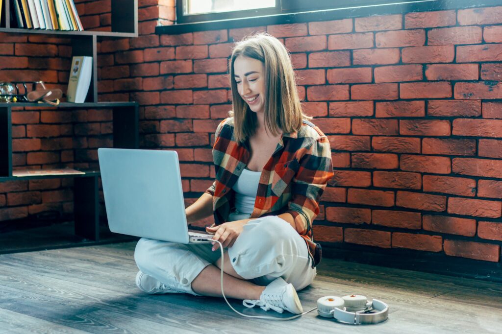 Young female student sitting on the floor working on a laptop.