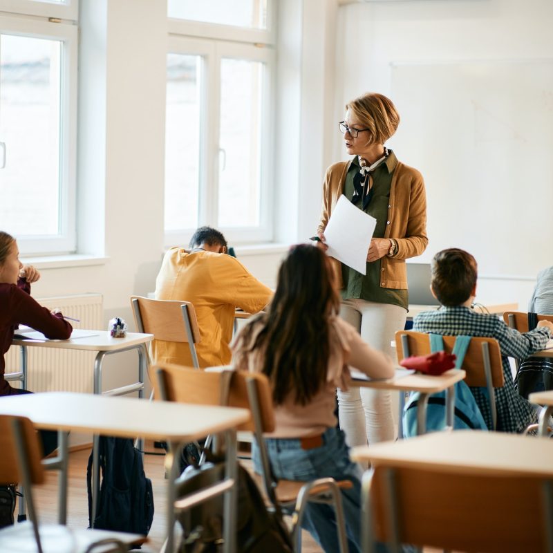 Mature teacher holding a class to group of school kids at primary school.